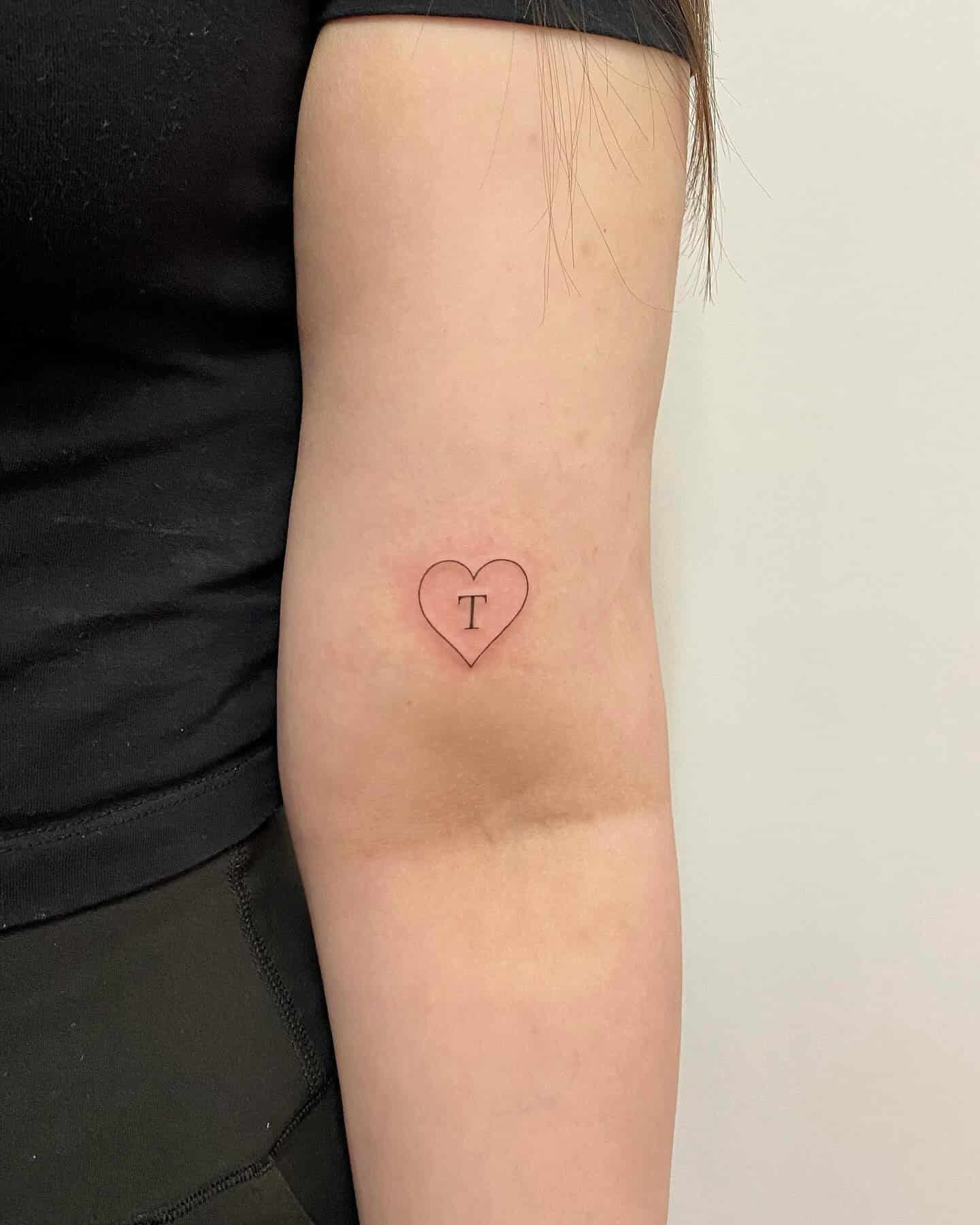 31] Heart Tattoo Above Elbow with ‘T’: Tribute